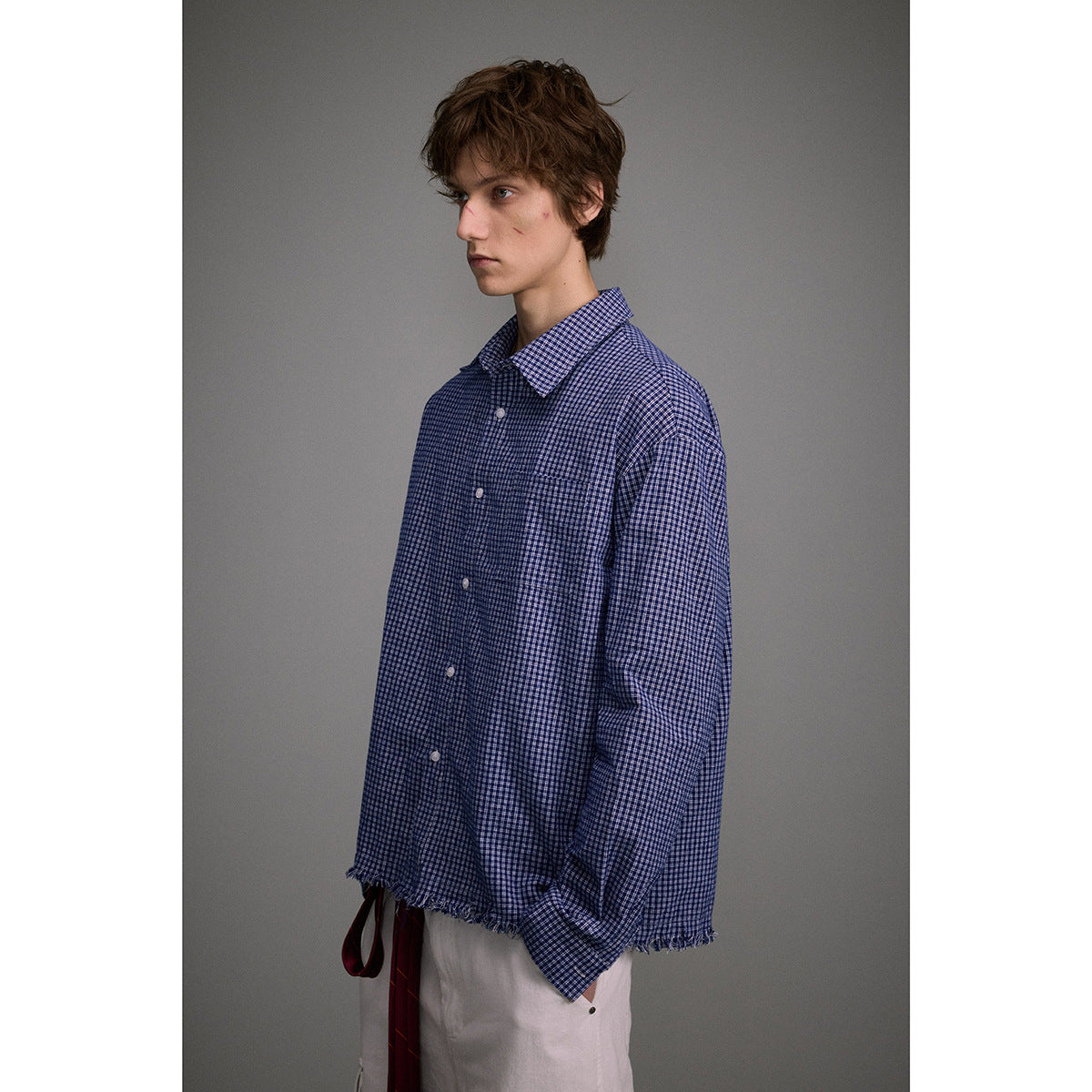 Side view of a model wearing a blue small-check button-up shirt with a frayed hem and white cargo pants.