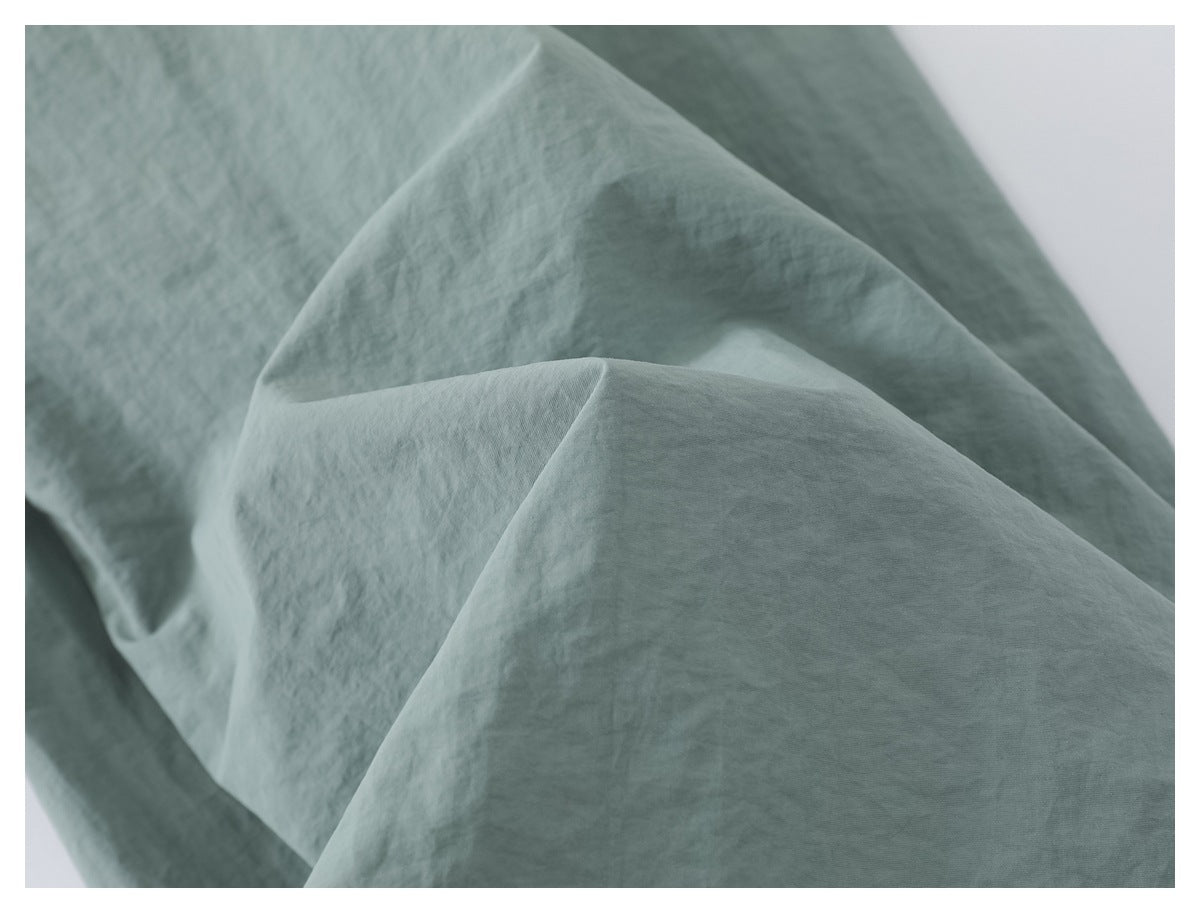 Close-up of pale sage fabric draped in soft folds, showing its surface texture.