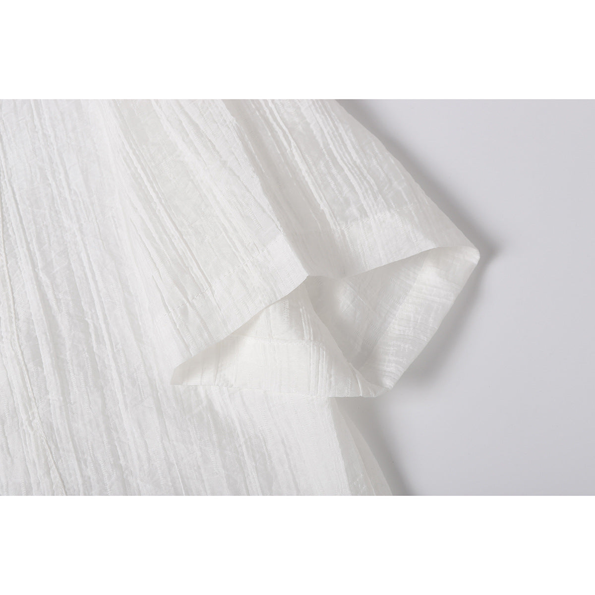 Close-up of the white shirt's short sleeve and hem, showing its textured fabric.