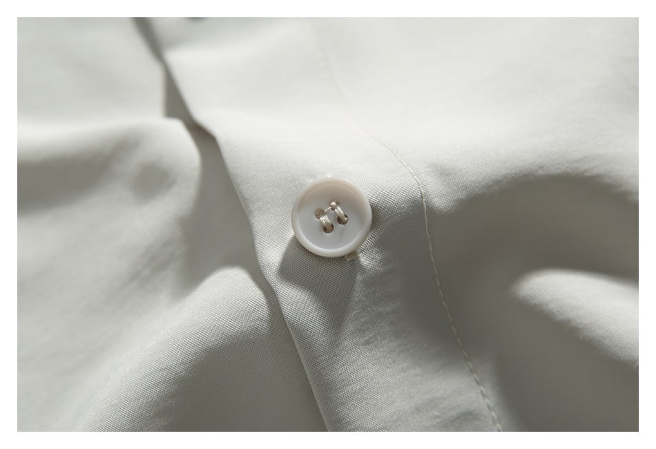 Close-up of a pale four-hole button and stitching on light ivory shirt fabric.