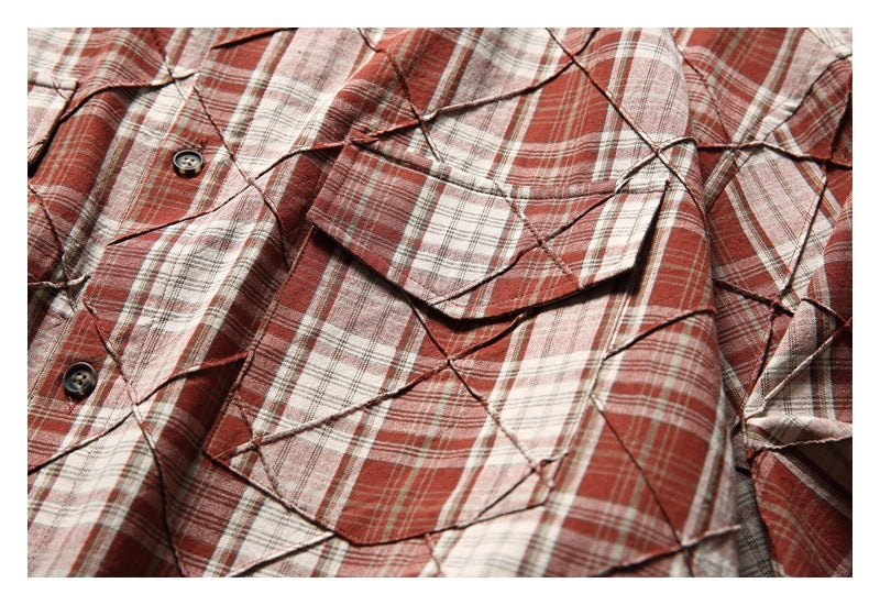 Close-up of a button and layered flap pocket on the red, cream, and gray plaid shirt.