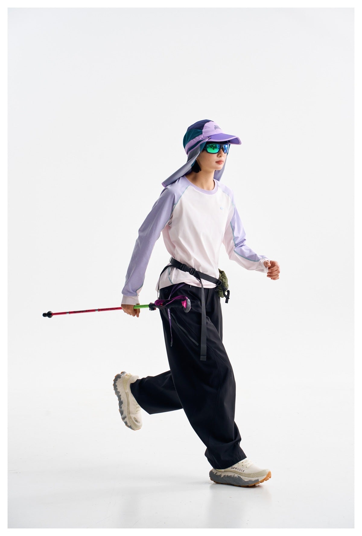 Model in a white long-sleeve top with lavender sleeves and dark wide-leg pants, wearing a sun hat and sunglasses.