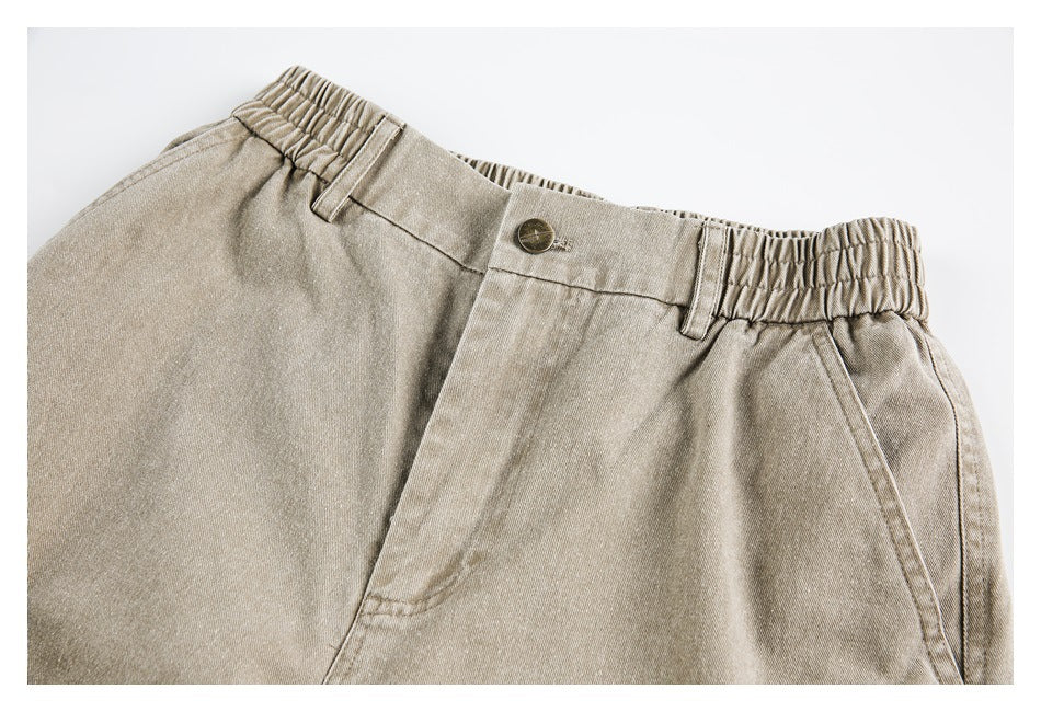 Close-up of beige pants showing the elastic waistband, belt loops, button, and front pocket.