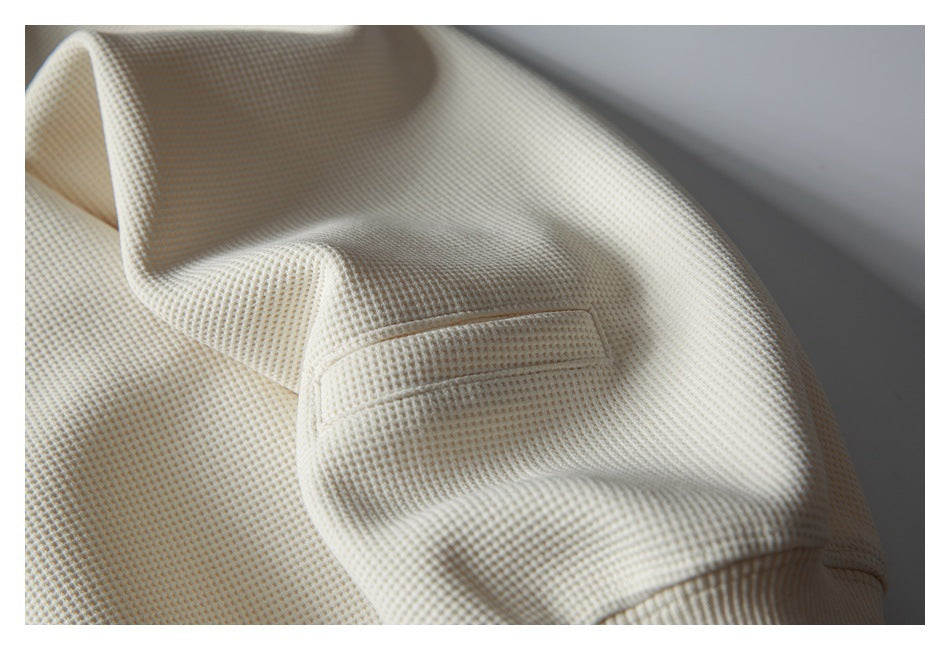 Close-up of the ivory sweatshirt sleeve showing textured fabric, a small stitched detail and ribbed cuff.