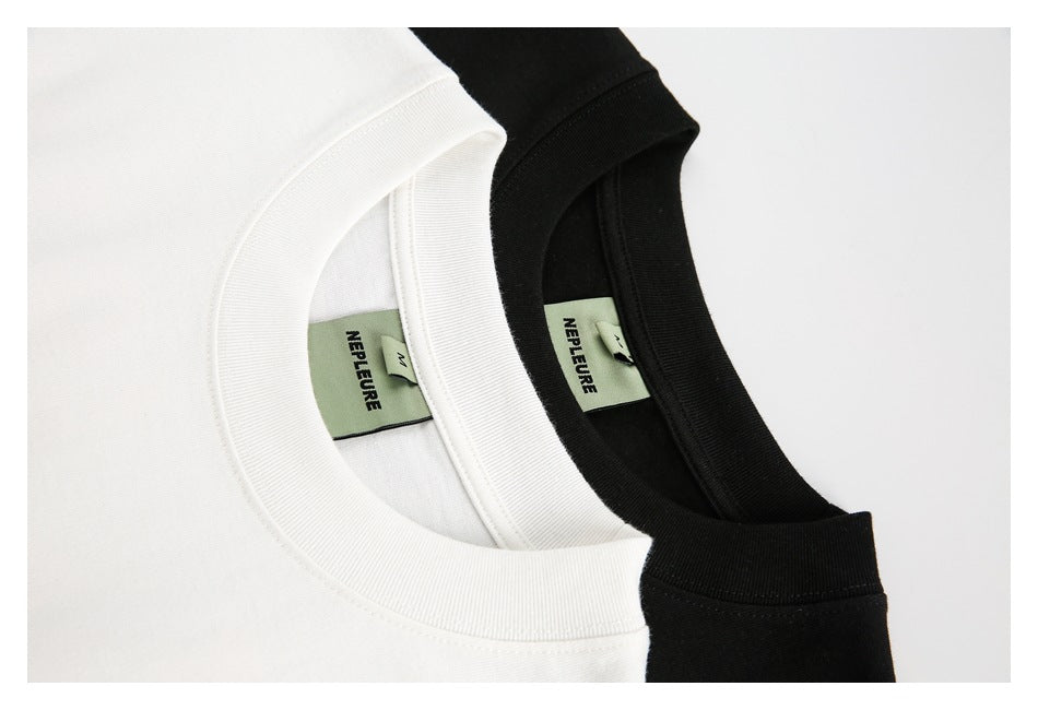 Close-up of white and black T-shirt ribbed crew necks with sewn-in green brand and size labels.