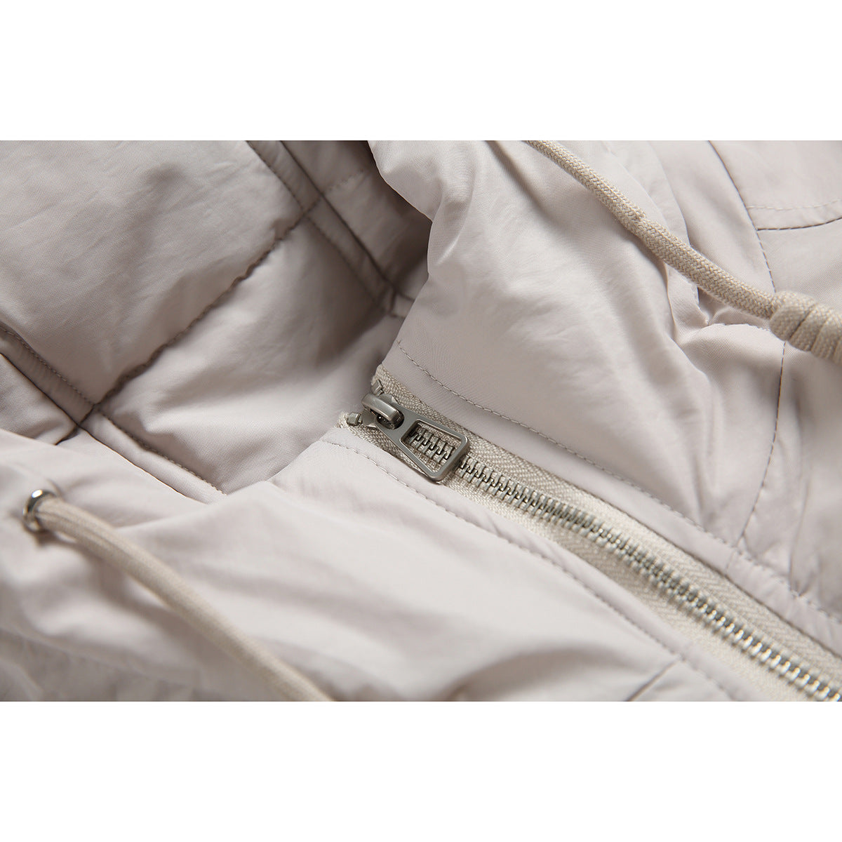 Close-up of the jacket's metal zipper, hood drawcord, and light beige fabric.