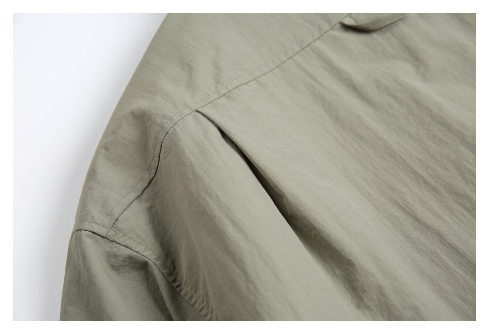 Close-up of a gray-green jacket shoulder showing curved seams and a pleat.