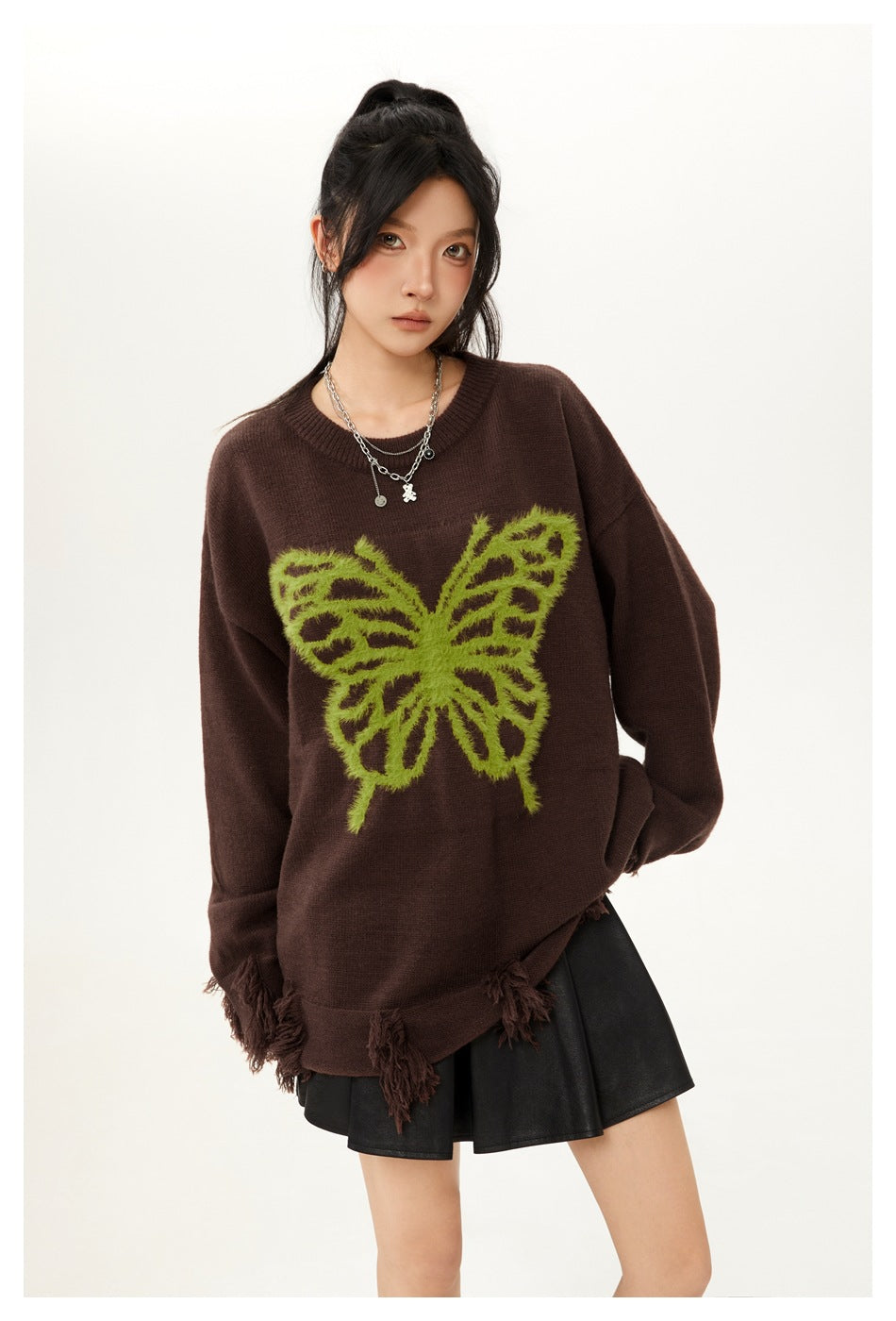 Model wearing a dark brown oversized sweater with a lime-green butterfly and tasseled hem, paired with a black skirt.