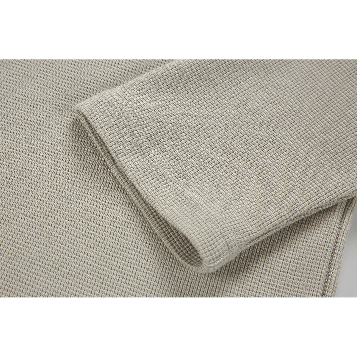 Close-up of a folded sleeve showing the light beige pullover's textured fabric and stitching.