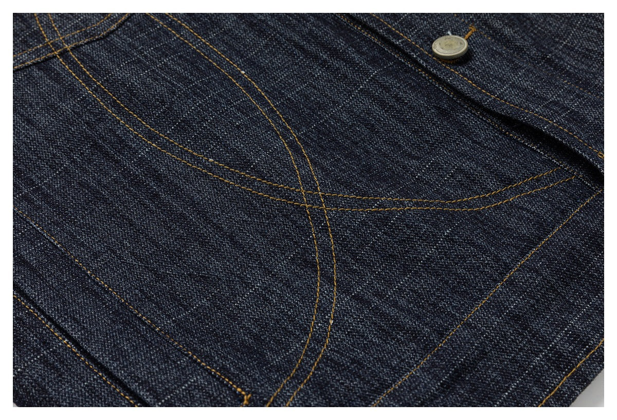 Close-up of dark indigo denim with curved ochre stitching and a metal button.