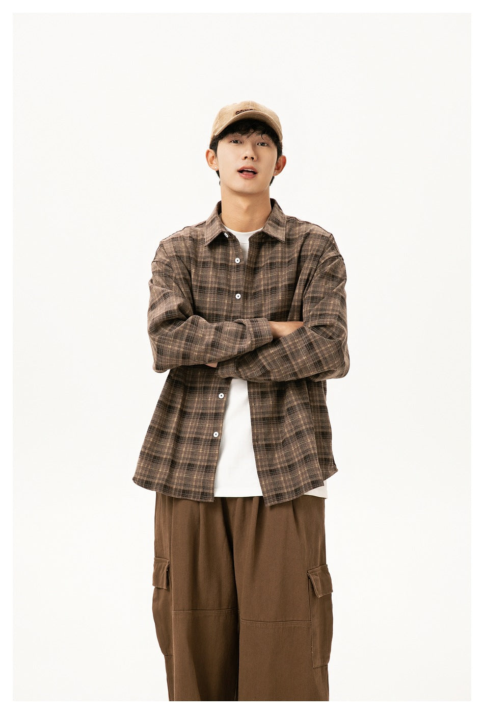 Model with arms crossed wearing a loose brown plaid button-up shirt over a white tee and brown cargo pants