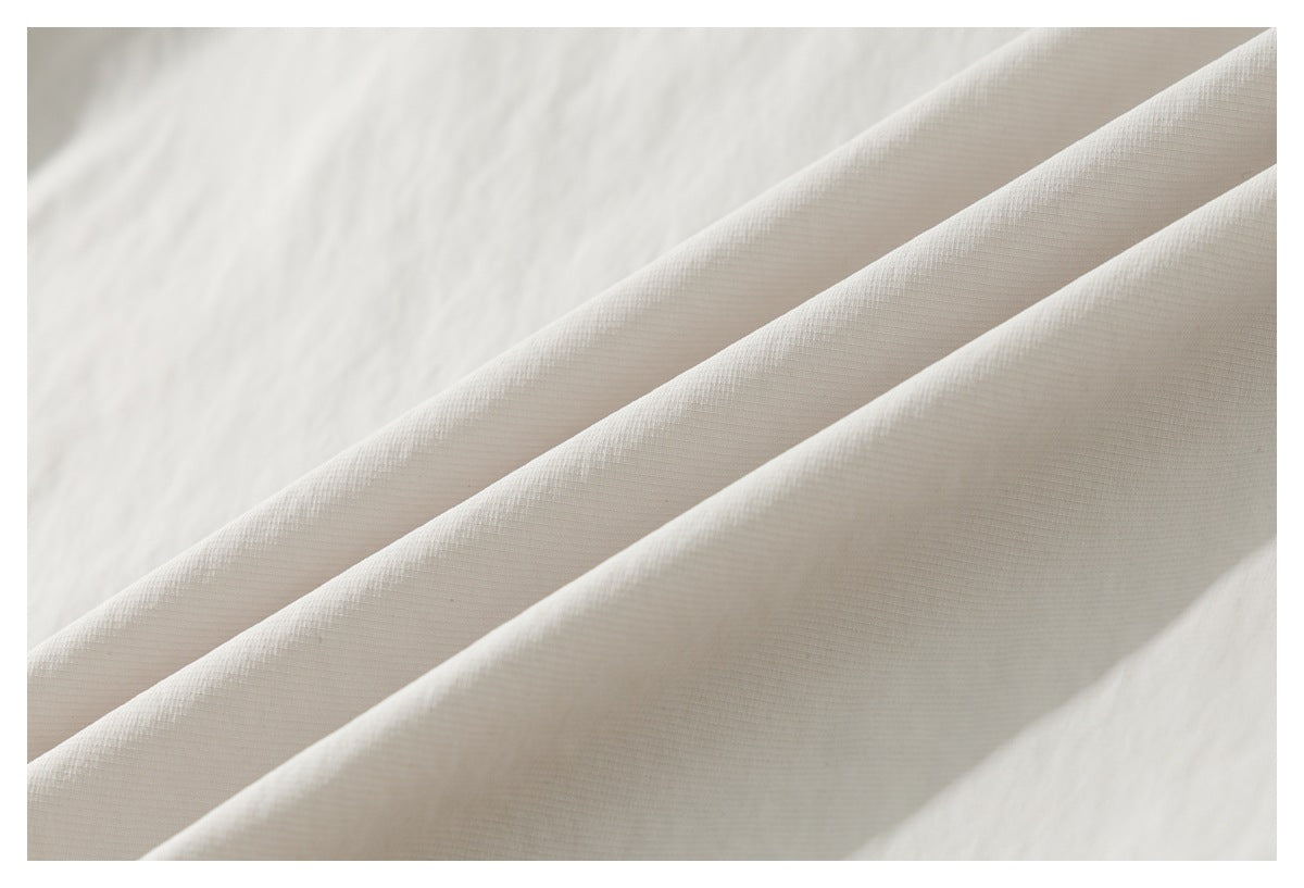 Close-up of off-white shirt fabric folded into soft diagonal pleats.