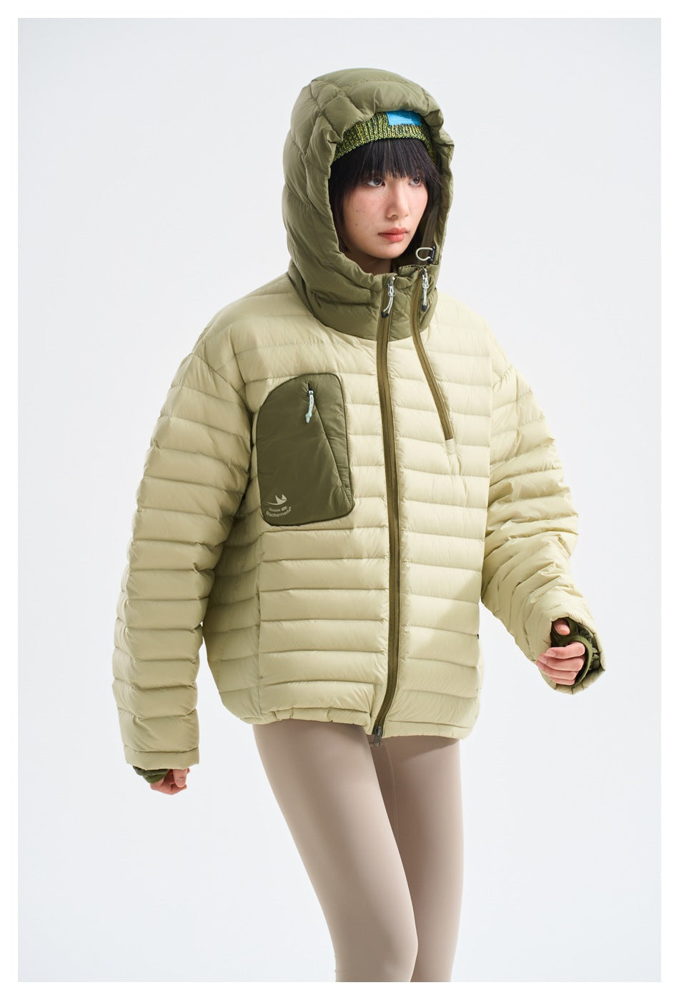 Three-quarter view of a model in a cream quilted jacket with an olive hood and chest pocket.