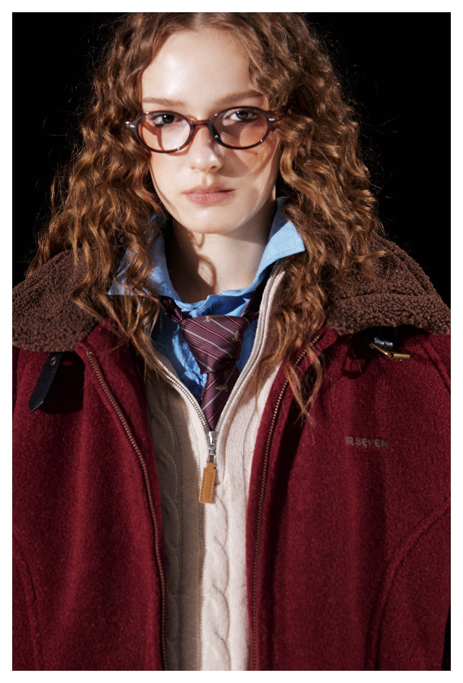 Close-up of a burgundy jacket’s brown fleece collar, zipper, and small embroidered chest logo.