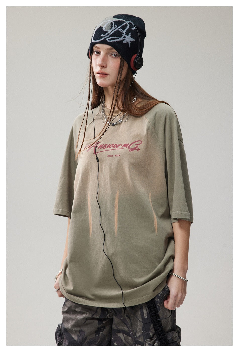 Three-quarter view of a model in a sage-green oversized graphic T-shirt with burgundy chest lettering.