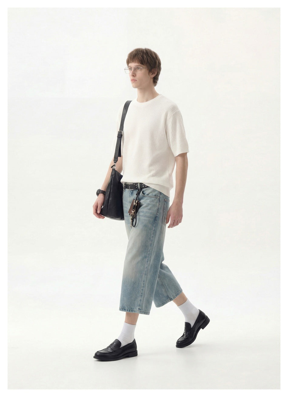Full-length side view of a model wearing a white textured short-sleeve shirt and light-wash denim shorts.