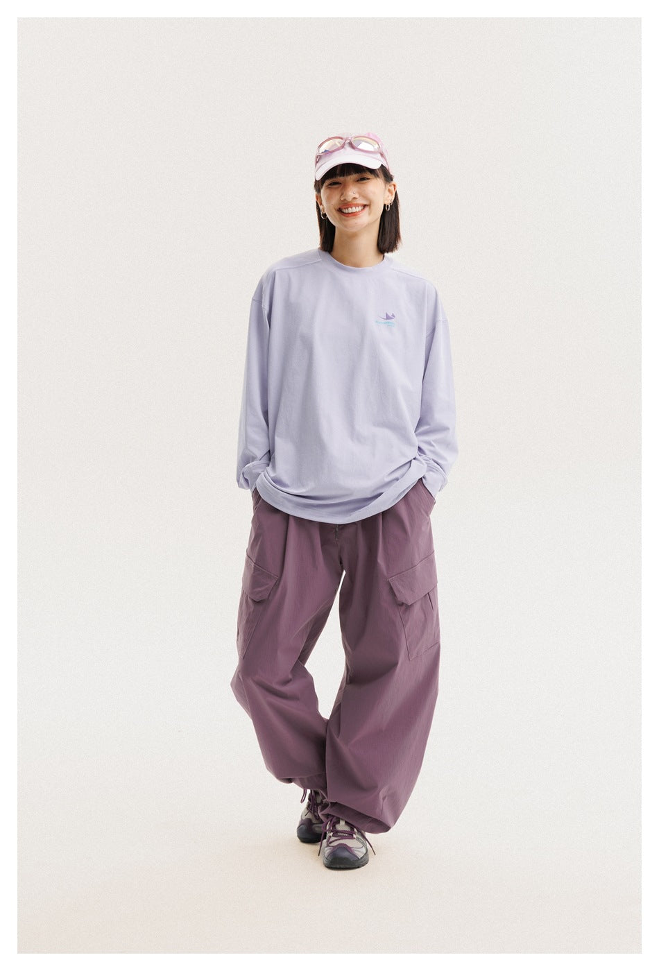 Model wearing a loose lavender long-sleeve shirt and mauve cargo pants, standing with hands in pockets.