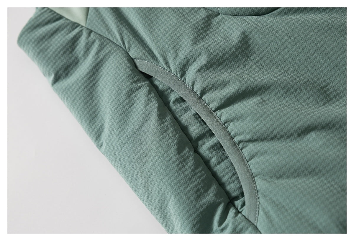 Close-up of a curved pocket opening and stitched textured panels on a sage-green jacket.
