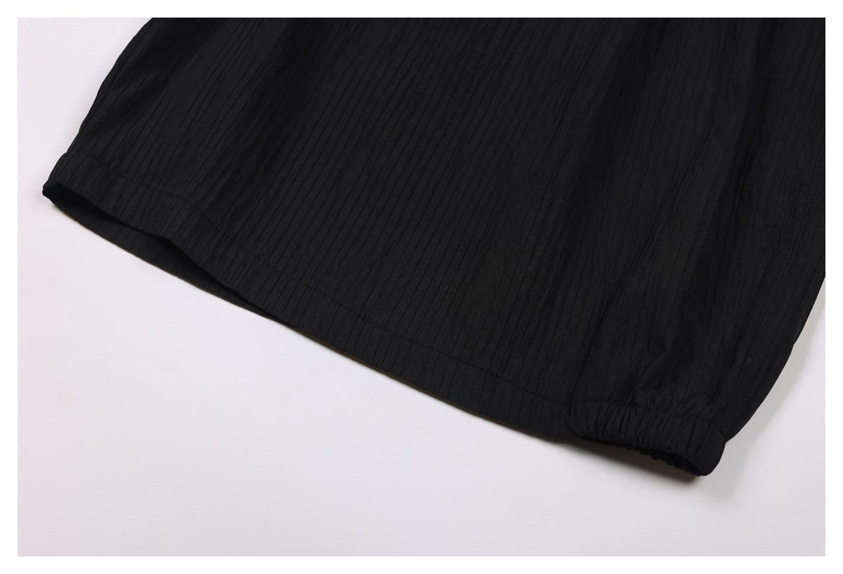 Close-up of black vertically ribbed garment fabric with a stitched hem and gathered edge.