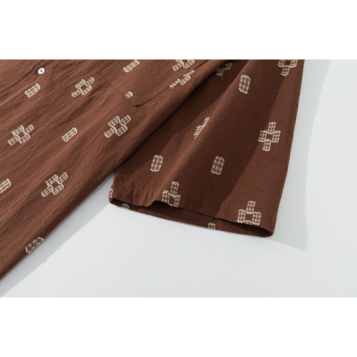 Close-up of the brown shirt's short sleeve and hem, showing repeating cream geometric motifs.