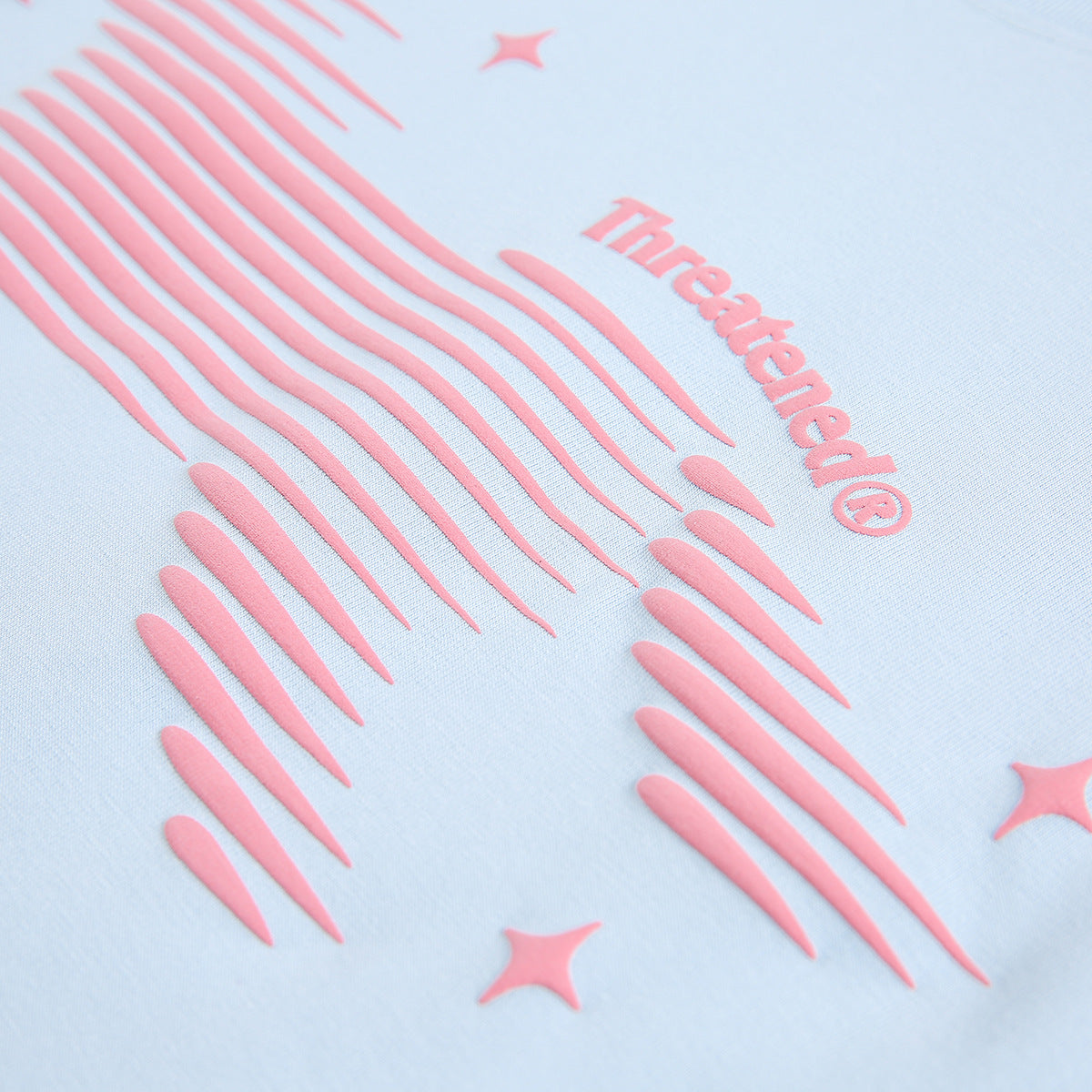 Close-up of a raised pink graphic and wordmark on pale blue T-shirt fabric.