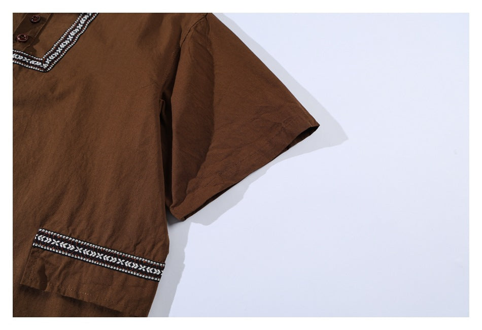 Partial flat-lay view of a brown short-sleeve shirt, showing its patterned placket trim and trimmed sleeve cuff.