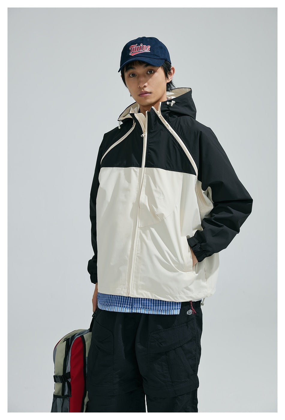 Front view of a model wearing a black-and-cream hooded jacket with a front zipper and chest pocket.