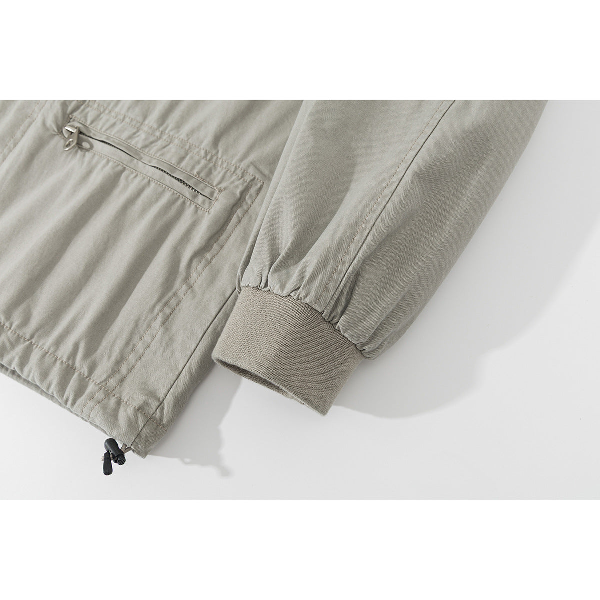 Close-up of a light gray jacket's zip pocket, gathered sleeve, ribbed cuff, and adjustable hem cord.