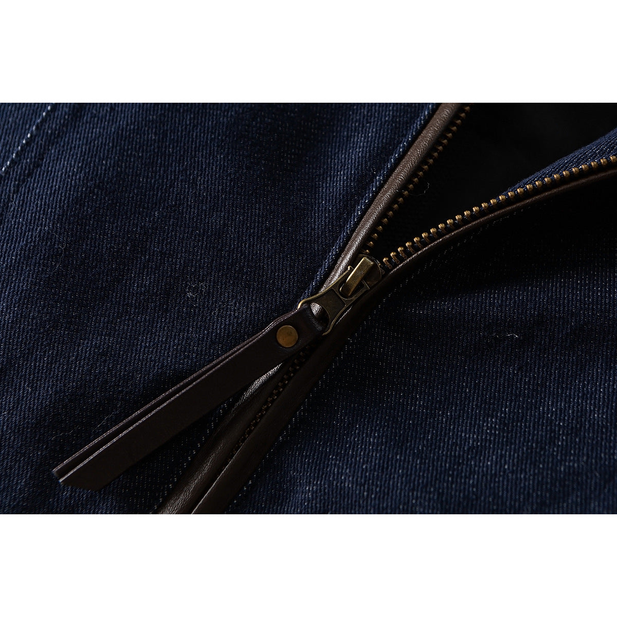 Close-up of the dark indigo jacket's brass zipper and long brown pull tab.