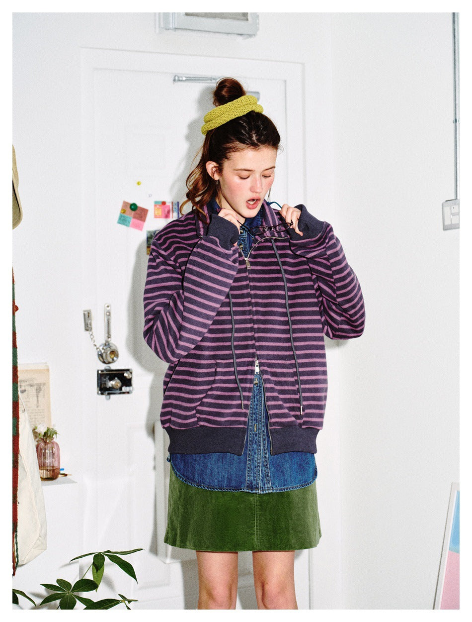 Model in the purple striped zip jacket with a denim shirt and green skirt, looking down while holding glasses