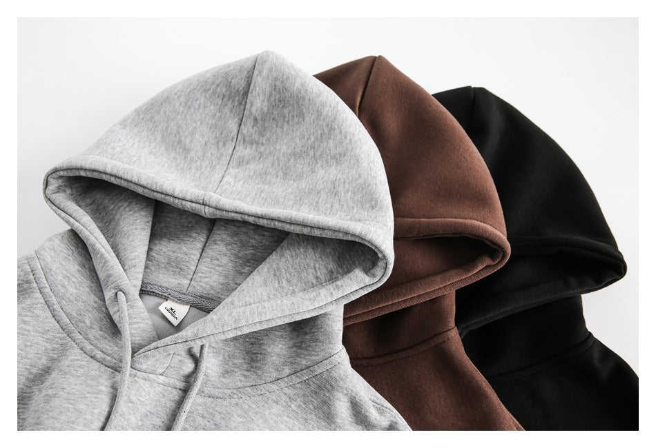 Close-up of three hoodies arranged together in light gray, brown, and black, showing their hoods and drawstrings.