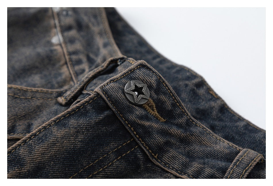 Close-up of a decorative button and waistband on dark washed denim with tan stitching.