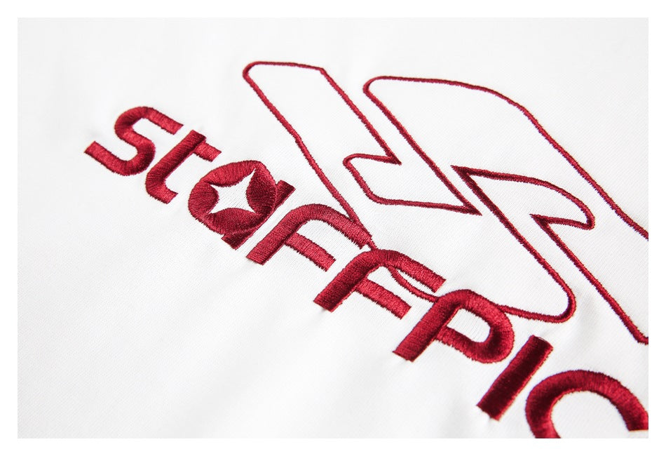 Tight close-up of red embroidered lettering and an outlined emblem on white fabric.