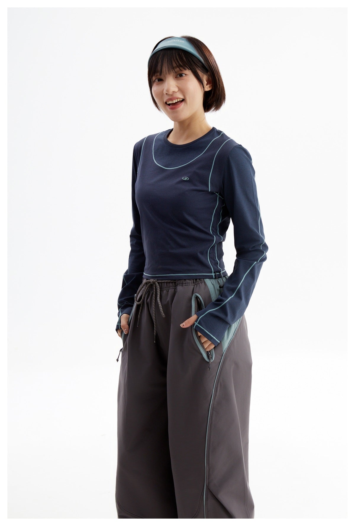 Model wearing a navy long-sleeve top with teal piping and charcoal wide-leg pants, shown from the front.