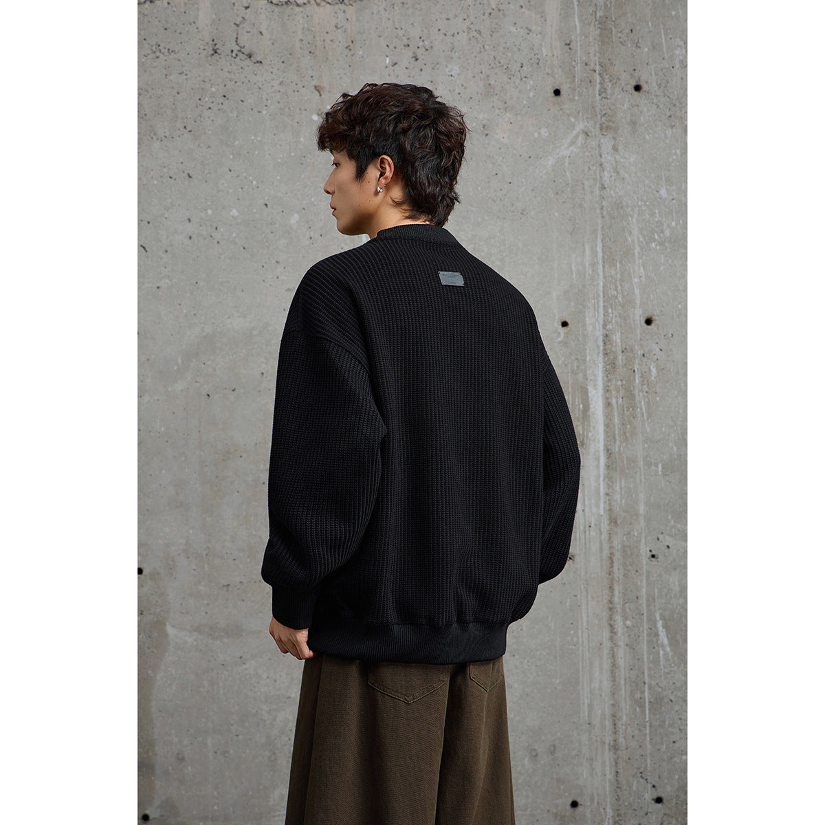 Rear view of a model wearing an oversized black textured sweater with ribbed cuffs and hem.