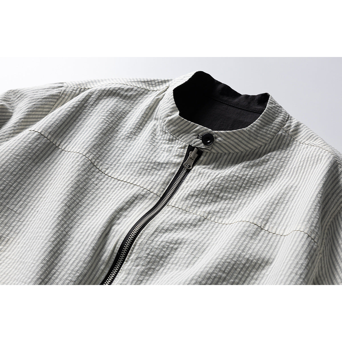 Close-up of a light gray pinstriped jacket with a black stand collar, button, and front zipper.