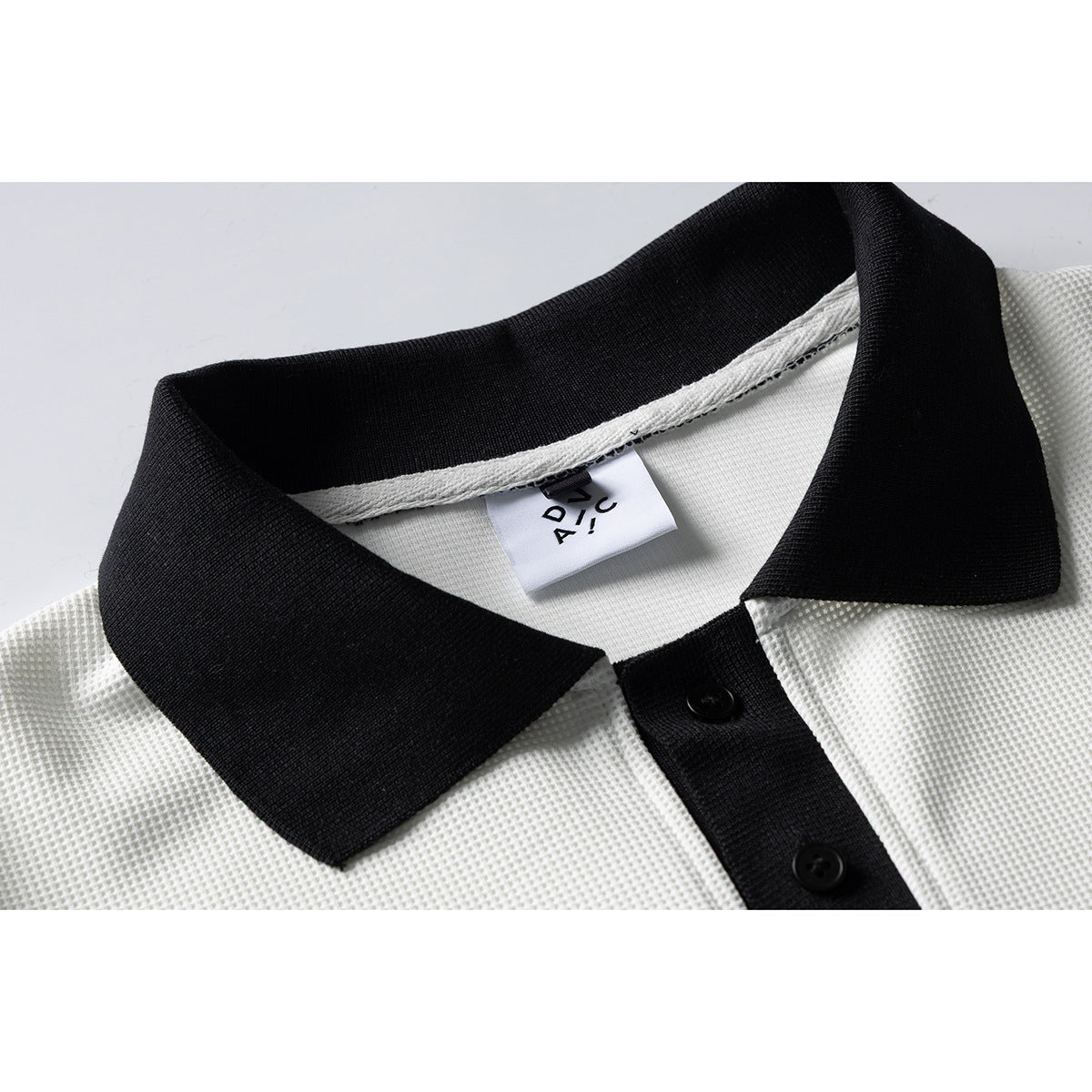 Close-up of a white textured polo shirt with a black collar and button placket; a sewn neck label is visible.