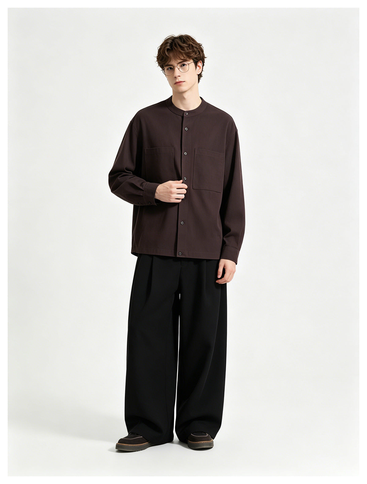 Model wearing a dark brown button-front band-collar shirt with two chest pockets, paired with wide black trousers.