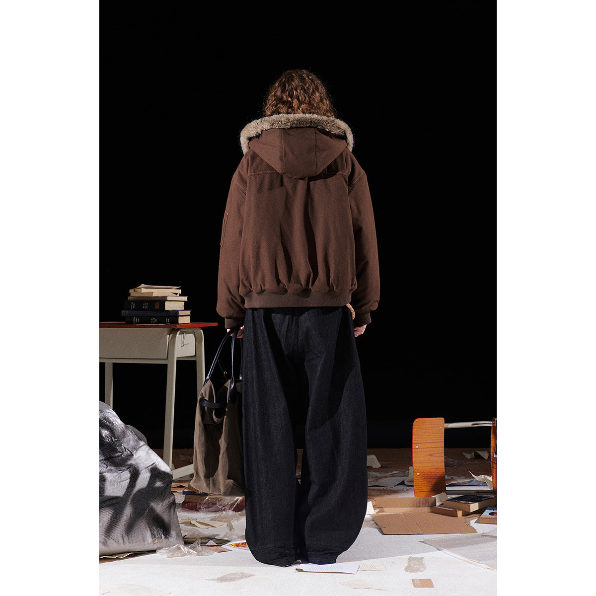 Back view of a model wearing a brown hooded jacket with a fur-trimmed hood and ribbed hem.