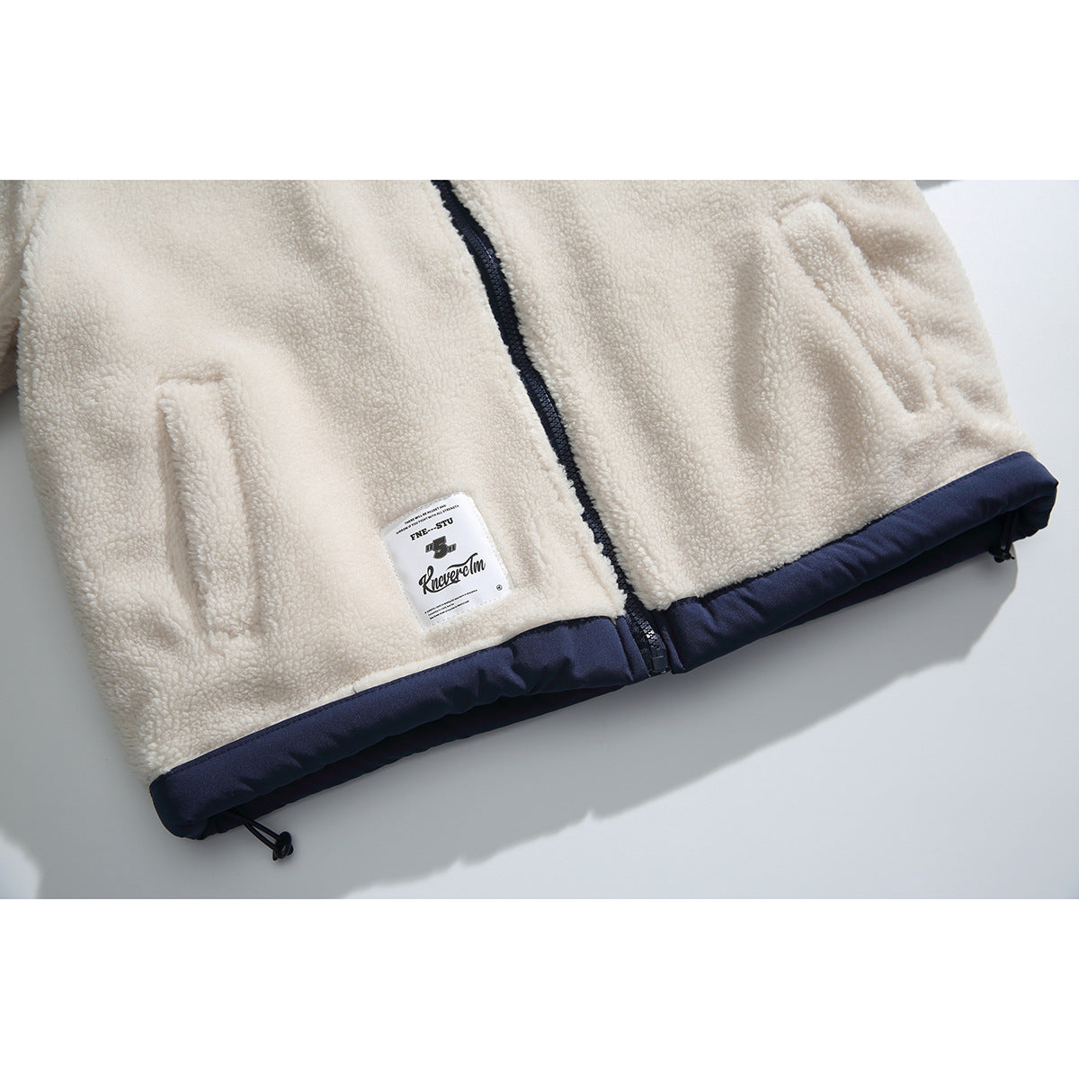 Close-up of the jacket's lower front, showing zip pockets, a navy hem, and an attached label.