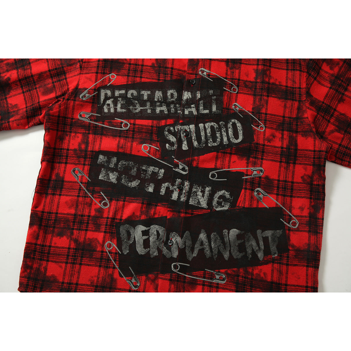 Close-up of the red-and-black plaid shirt’s black graphic panels, distressed English lettering, and safety-pin artwork.