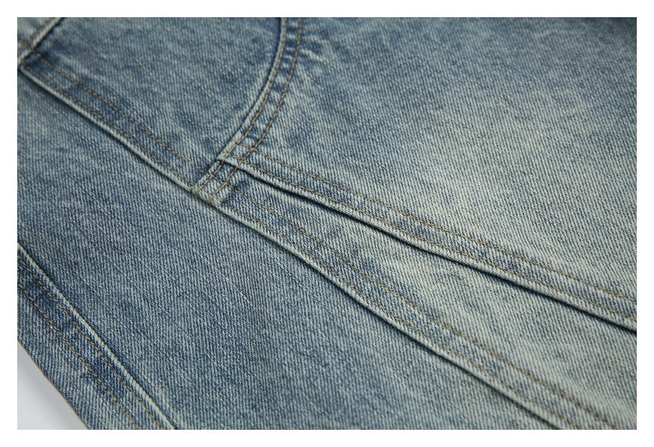 Close-up of light blue washed denim with intersecting seams and tan stitching.