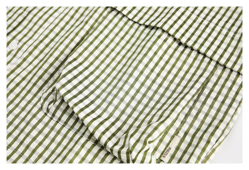 Close-up of the chest pocket and olive-and-white checked pattern on a laid-flat shirt.