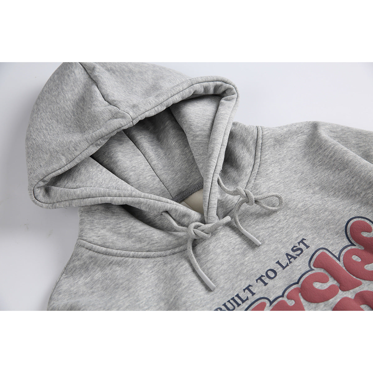 Close-up of a heather-gray hoodie showing its lined hood, drawstrings, and part of a red and navy chest print.