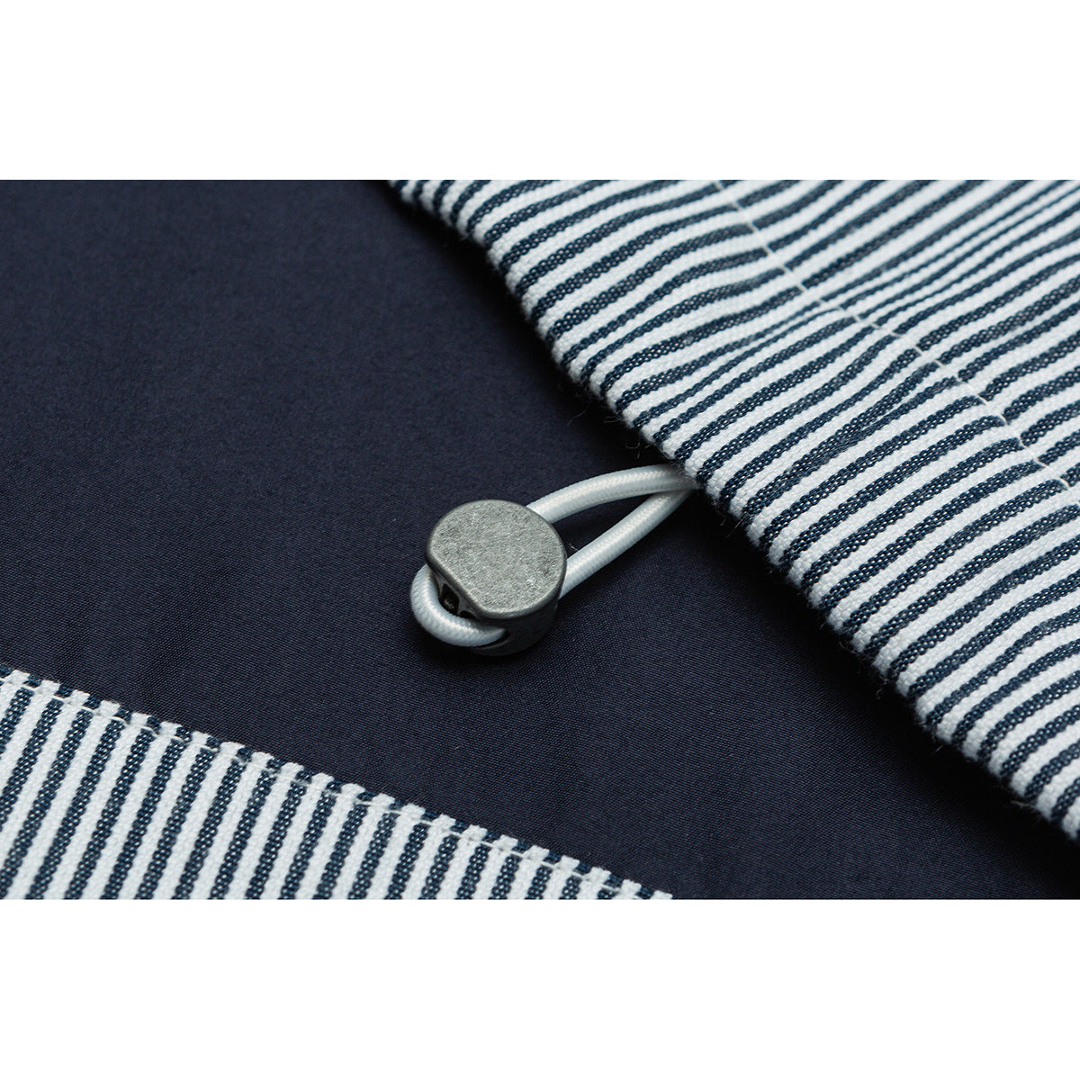 Close-up of a jacket's white cord toggle fastening between navy fabric and striped panels.