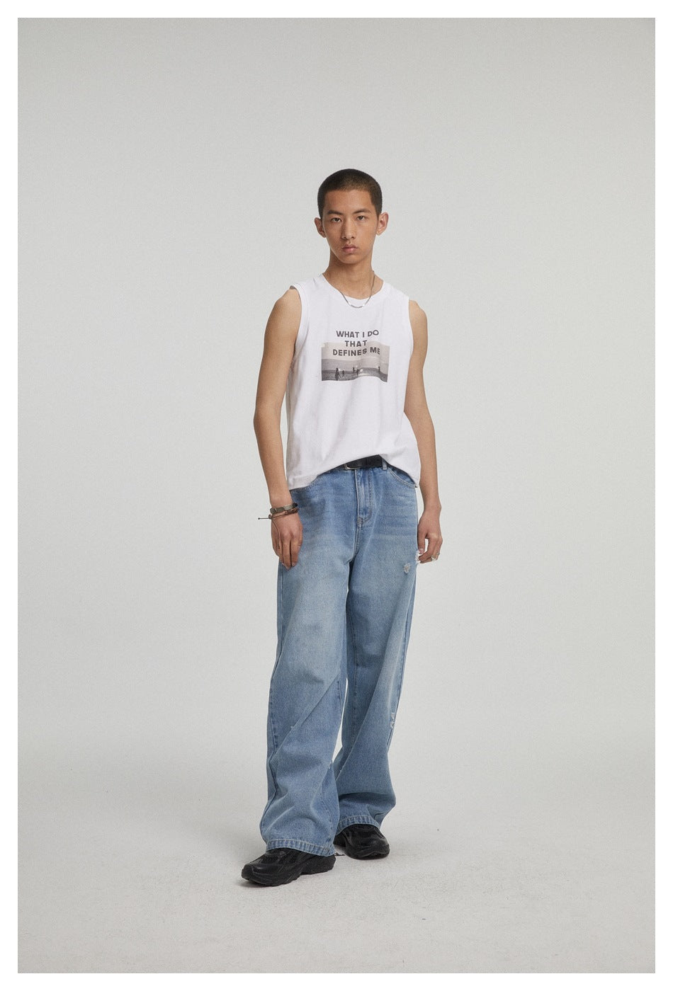 Front view of a model wearing a white graphic sleeveless shirt and loose distressed blue jeans.