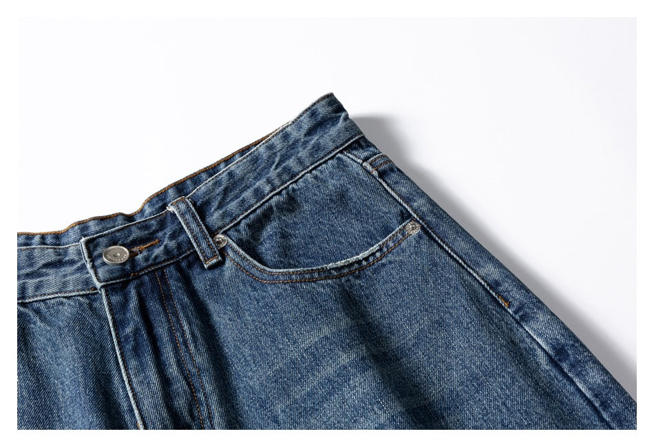 Close-up of the waistband, button, belt loop, and right front pocket of blue washed jeans.