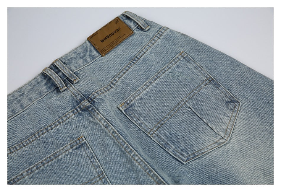 Close-up of light-wash jeans showing the waistband, belt loops, back pockets, and a brown leather patch.