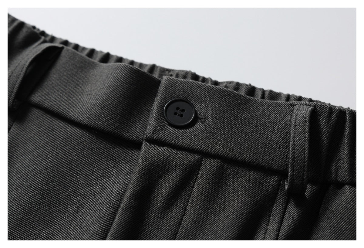 Close-up of dark trousers showing a black waist button, belt loop and gathered elastic waistband.