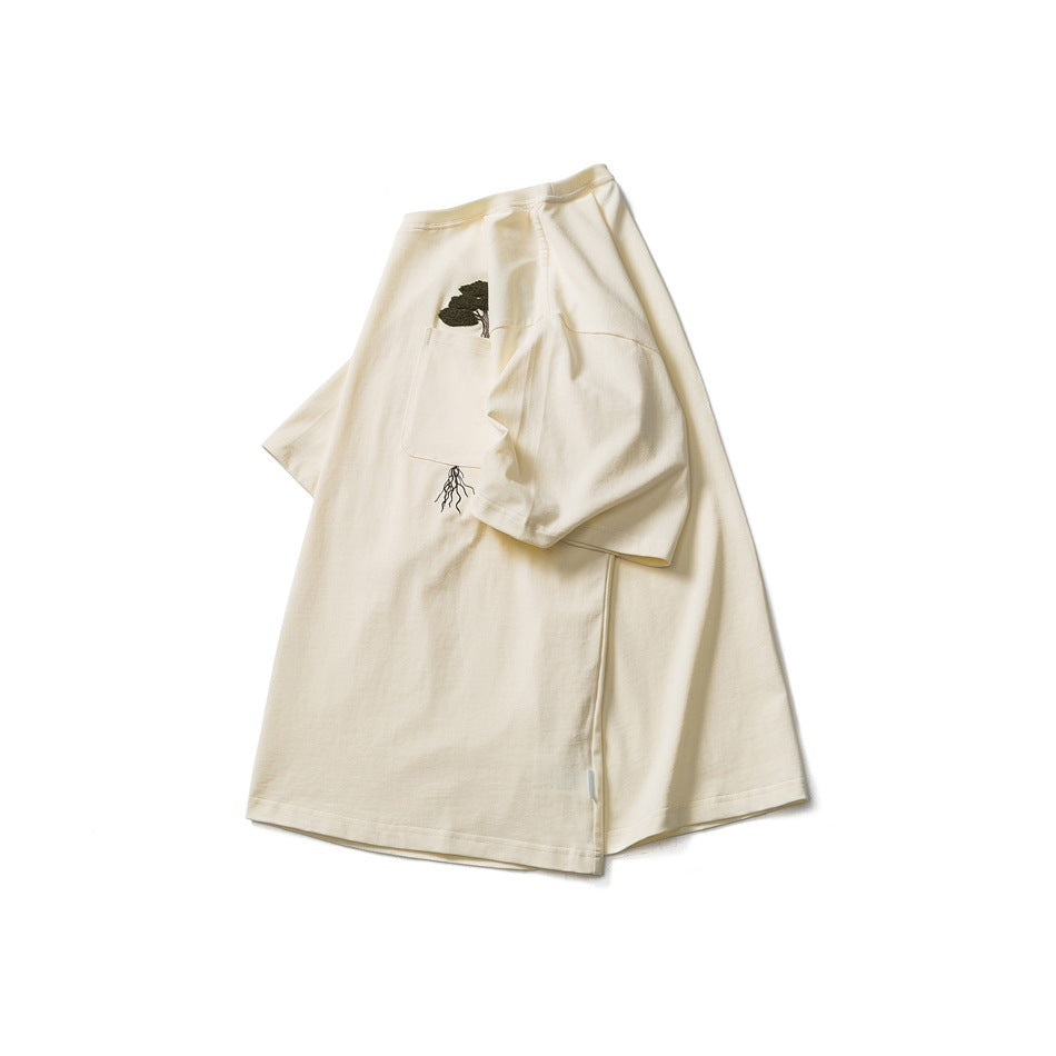 Ivory short-sleeve T-shirt displayed flat, with a chest pocket and dark embroidered tree motif.